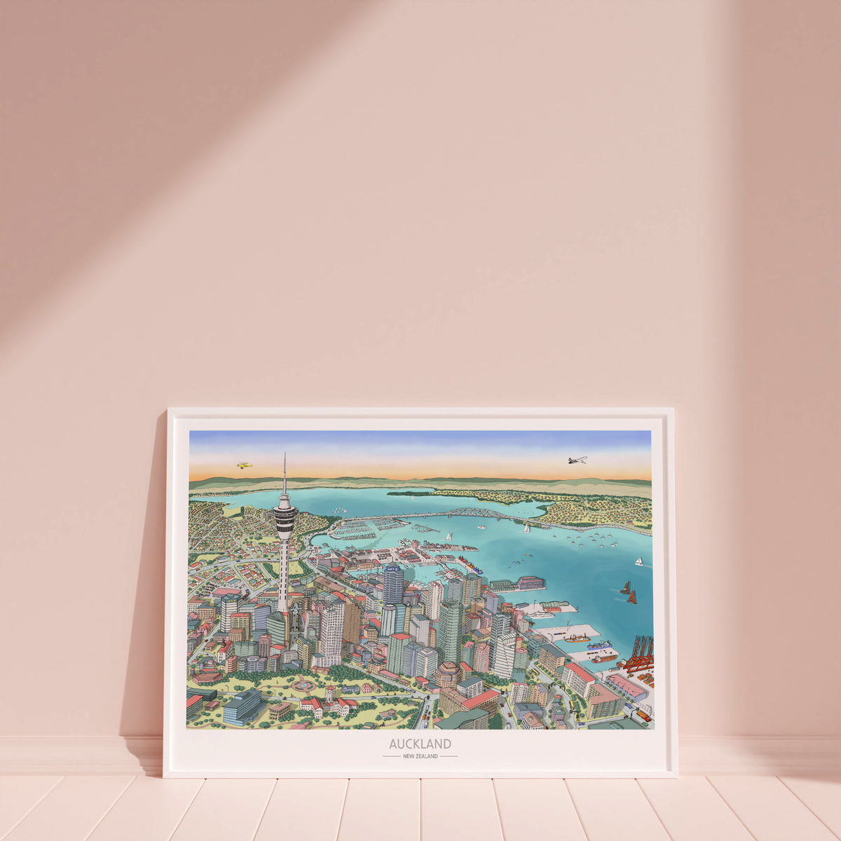 Hand-drawn Auckland map art print with digital colour, displayed in a white frame. Features Skytower, CBD, waterfront, docks, bridge, and America's Cup boats. New Zealand.