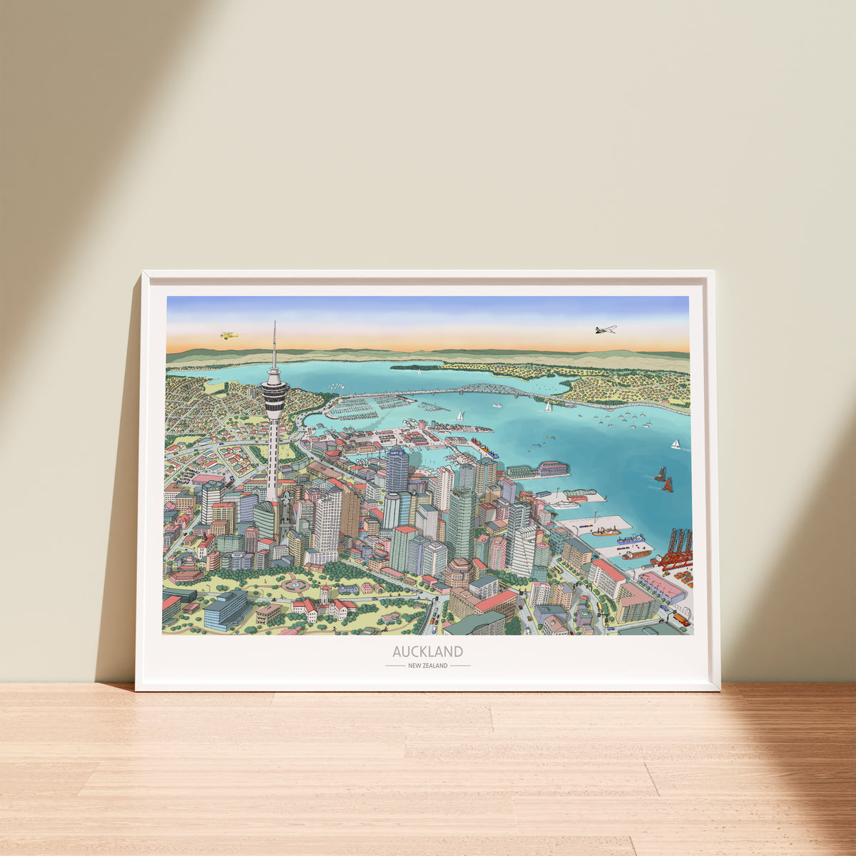 Hand-drawn Auckland map art print with digital colour, displayed in a white frame. Features Skytower, CBD, waterfront, docks, bridge, and America's Cup boats.