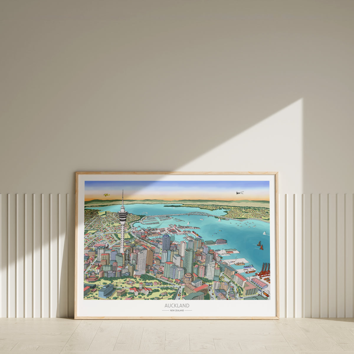 Hand-drawn Auckland map art print with digital colour, displayed in a wood frame. Features Skytower, CBD, waterfront, docks, bridge, and America's Cup boats.