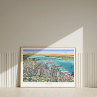 Hand-drawn Auckland map art print with digital colour, displayed in a wood frame. Features Skytower, CBD, waterfront, docks, bridge, and America's Cup boats.