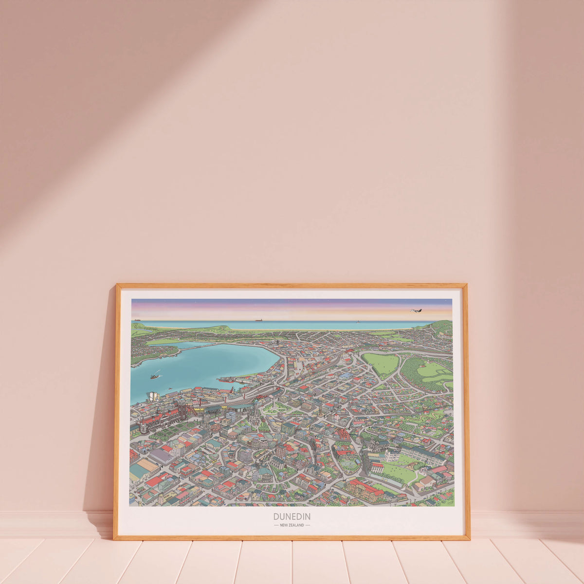 Hand-drawn map art print of Dunedin, New Zealand – detailed pen and digital colour, featuring the Octagon, city buildings, and ocean on the horizon. Wood frame version for display.