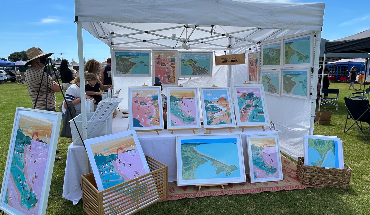 Market in Waihi Beach displaying Hand drawn map of Waihi Beach, New Zealand and Bowentown peninsula art print. The illustration highlights the also Athenree, boats, and people enjoying the beach.